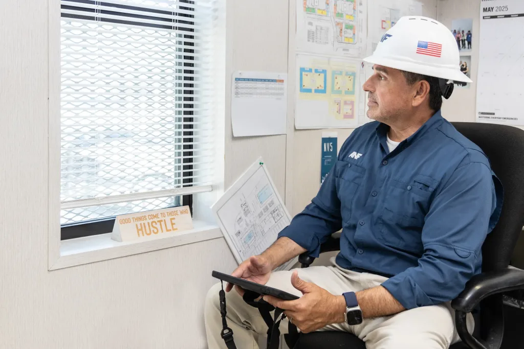ANF superintendent in a hard hat reviewing plans on a tablet in the site office